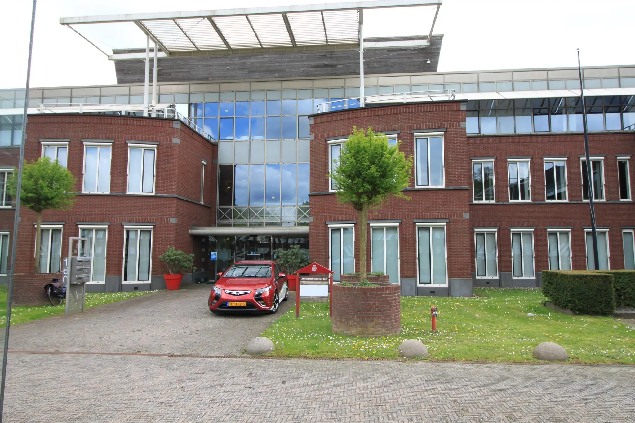 Vooraanzicht van een modern kantoorgebouw aan de Arnhemse Bovenweg met een rode auto geparkeerd voor de ingang.
